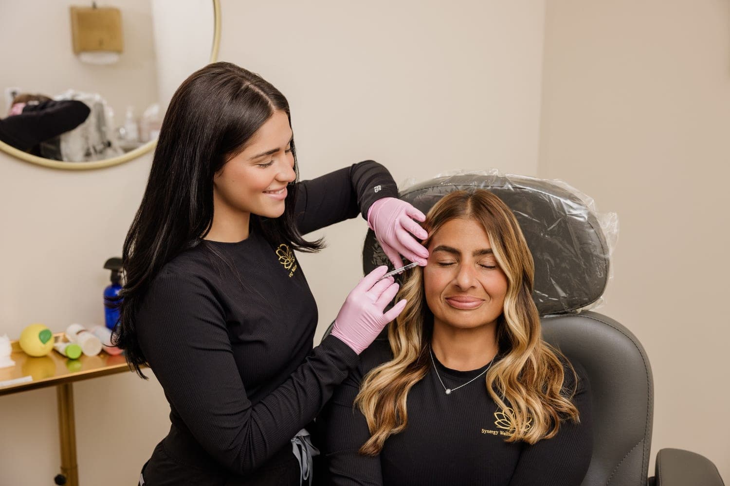 A Synergy injector performing a treatment for a seated, smiling client in the Oceanport studio.