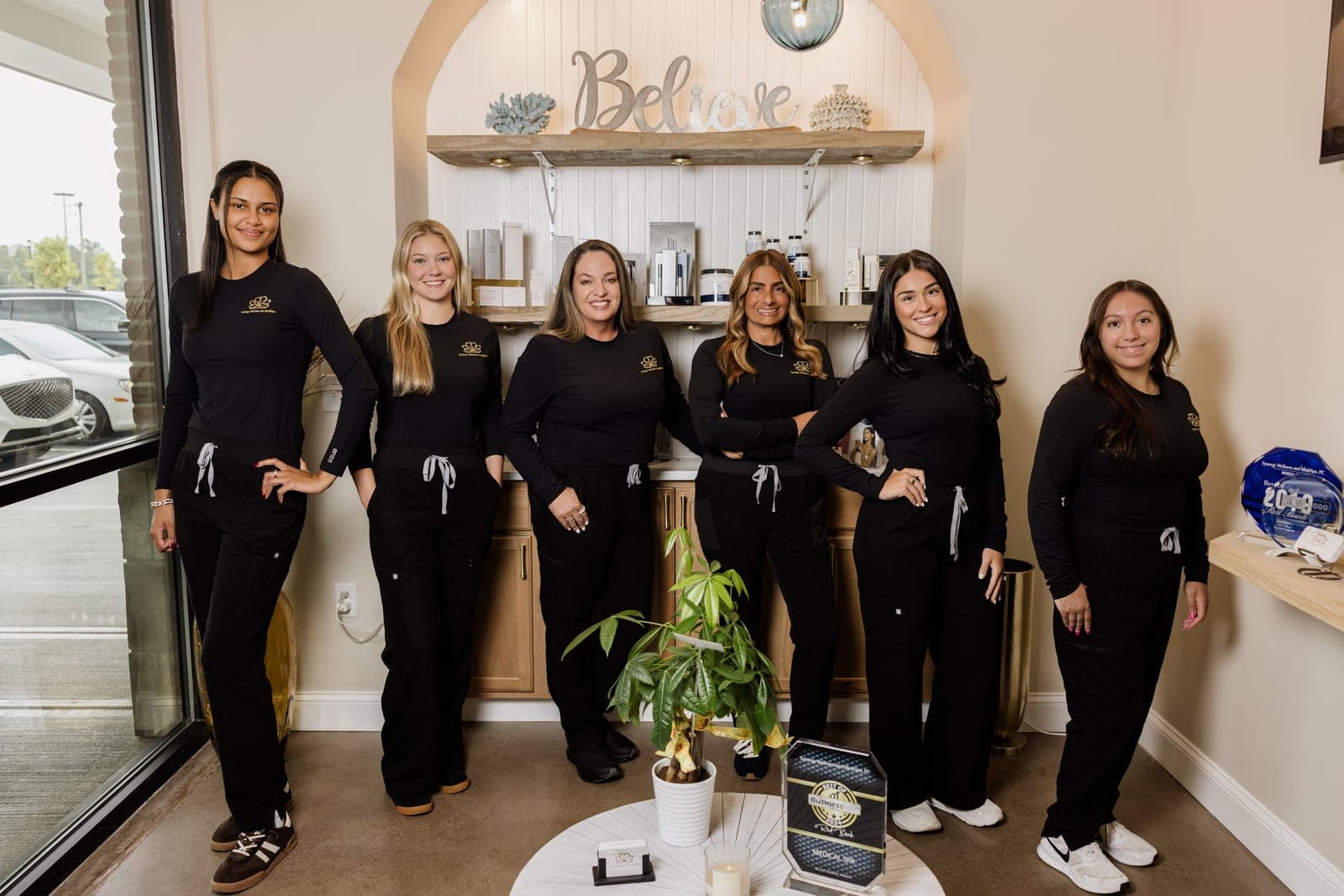 The Synergy Wellness and MediSpa team at the Oceanport reception, beneath the Believe sign.